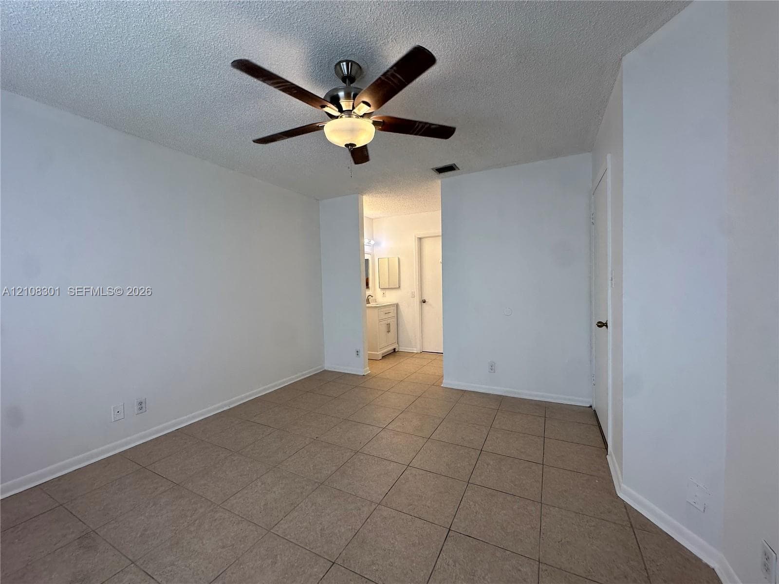 Spacious room featuring neutral tile flooring, a multi-blade ceiling fan with integrated lighting, and a textured ceiling finish