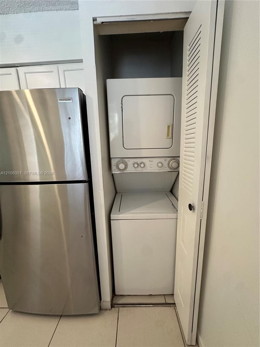 Stainless steel refrigerator paired with a stacked laundry unit enclosed in a louvered-door closet