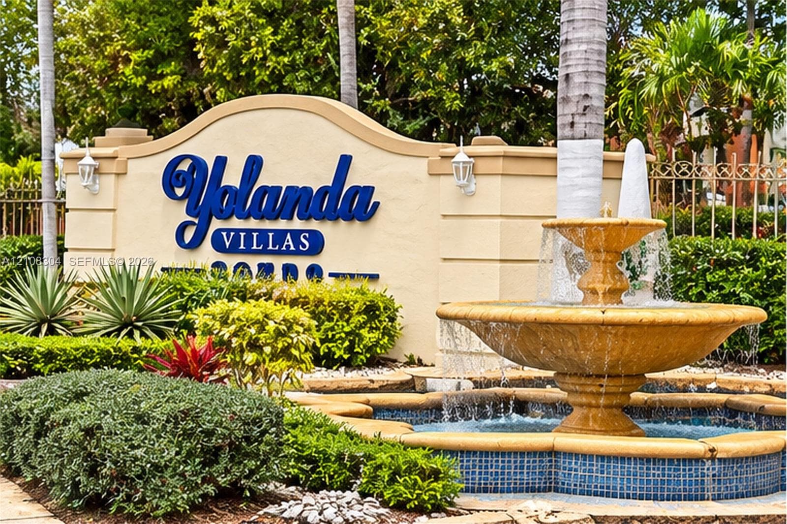 Stone monument signage with raised lettering, tiered stone fountain with blue tile accents, and established tropical landscaping