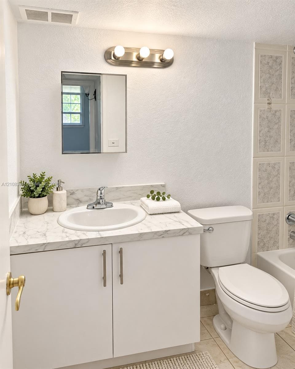 Bathroom featuring a vanity with a white cabinet, stone-finish countertop, undermount sink, three-light brushed nickel fixture, and rectangular mirror