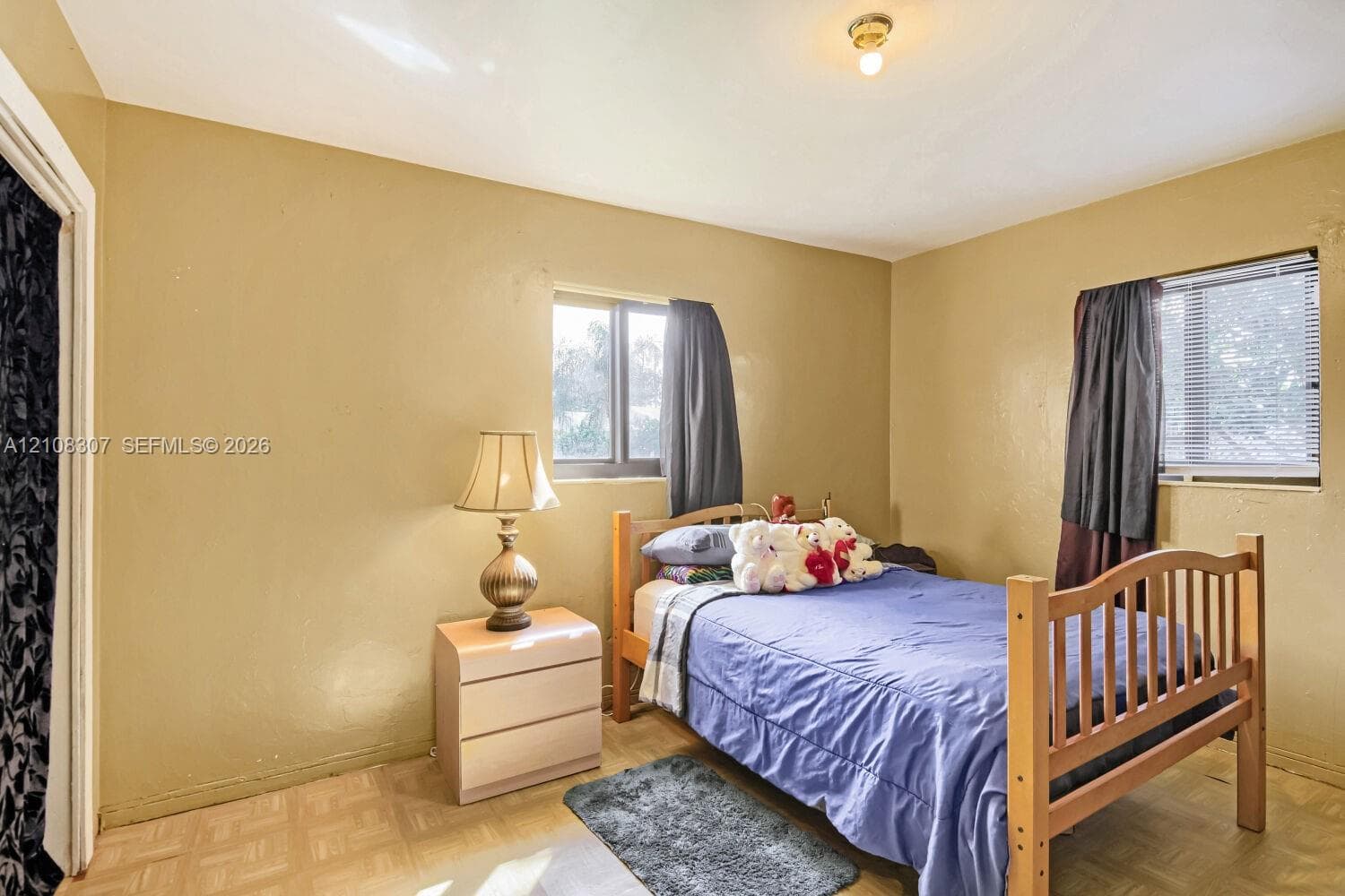 Bedroom featuring light-toned flooring, two windows providing natural light, and a ceiling-mounted light fixture