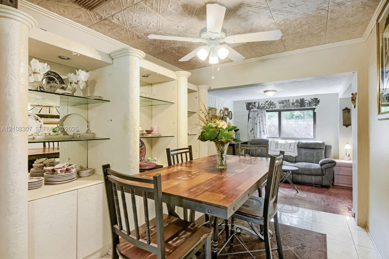 Custom built-in cabinetry with glass shelving and mirrored backing, decorative ceiling tiling, and architectural columns