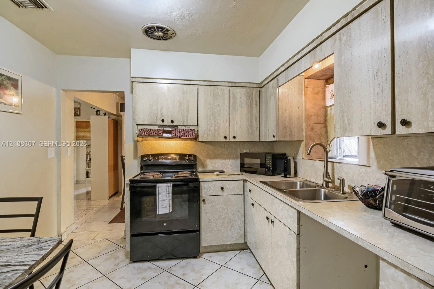 Kitchen featuring cabinetry with a stone-finish facade, stainless steel dual-basin sink, high-arc faucet, and tiled flooring