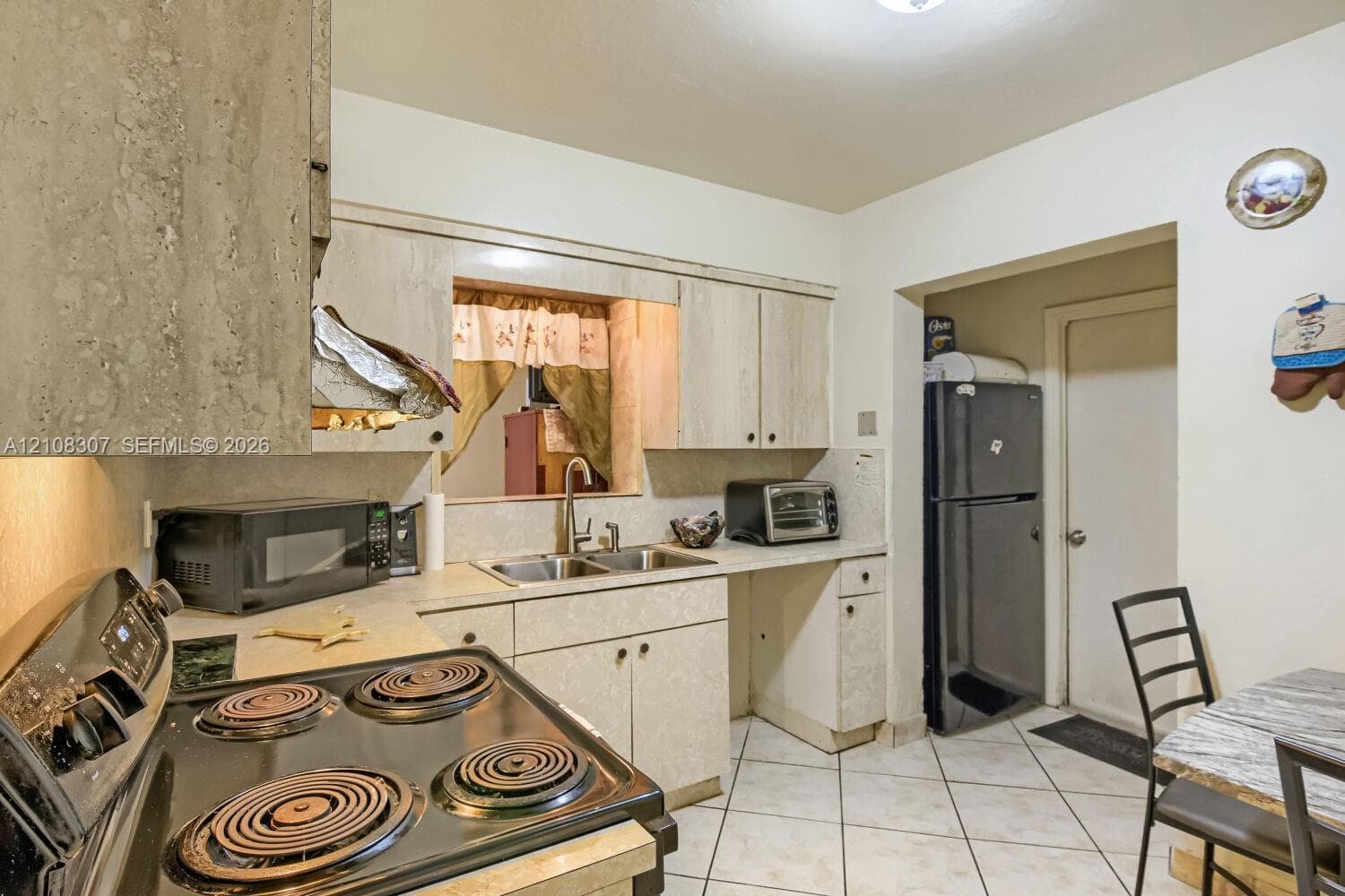 Kitchen featuring laminate cabinetry, dual-basin stainless steel sink, tile flooring, and a serving pass-through window