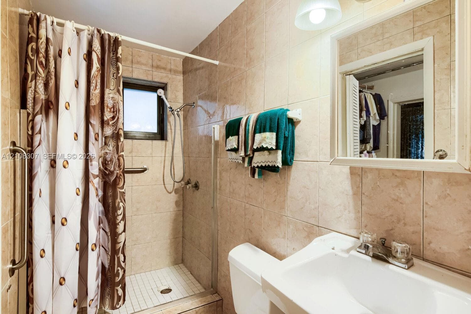Bathroom featuring full-height wall tiling, a walk-in shower with a glass door, a pedestal sink with a dual-handle faucet, and a wall-mounted medicine cabinet