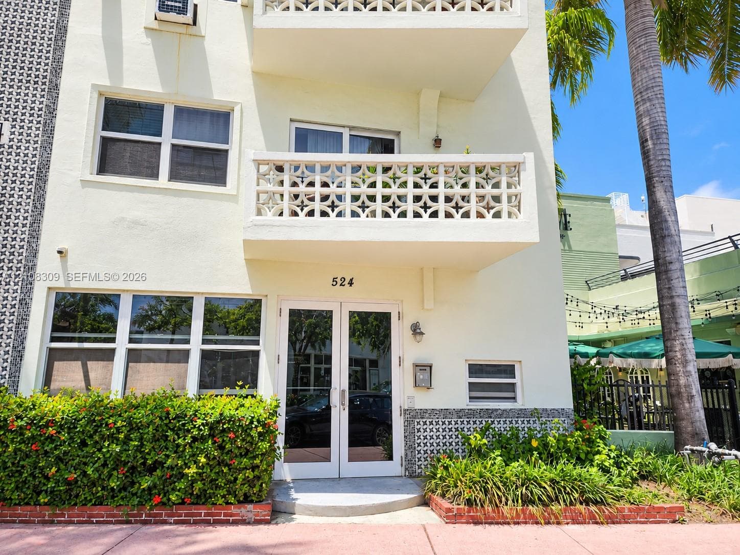 Exterior facade featuring decorative concrete masonry screen walls, private balcony, glass-paneled double entry door, and manicured landscaping with brick edging