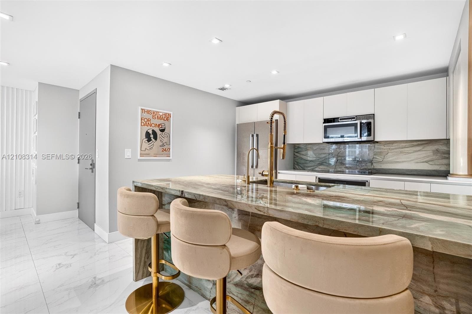 Kitchen featuring a stone waterfall island with a metal gooseneck faucet, white flat-panel cabinetry, a matching stone backsplash, stainless steel appliances, and large-format tile flooring