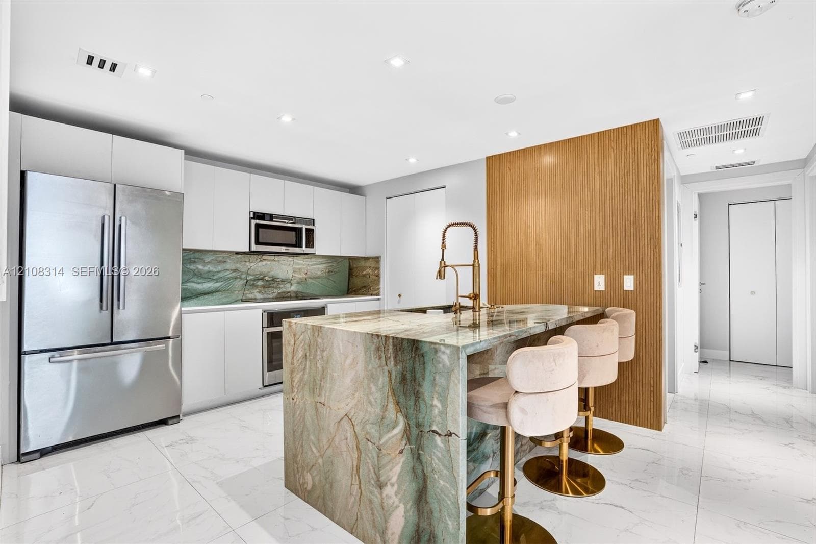 Kitchen featuring flat-panel white cabinetry, stone-clad waterfall island, matching stone backsplash, wood-finish accent wall, and stainless steel appliances