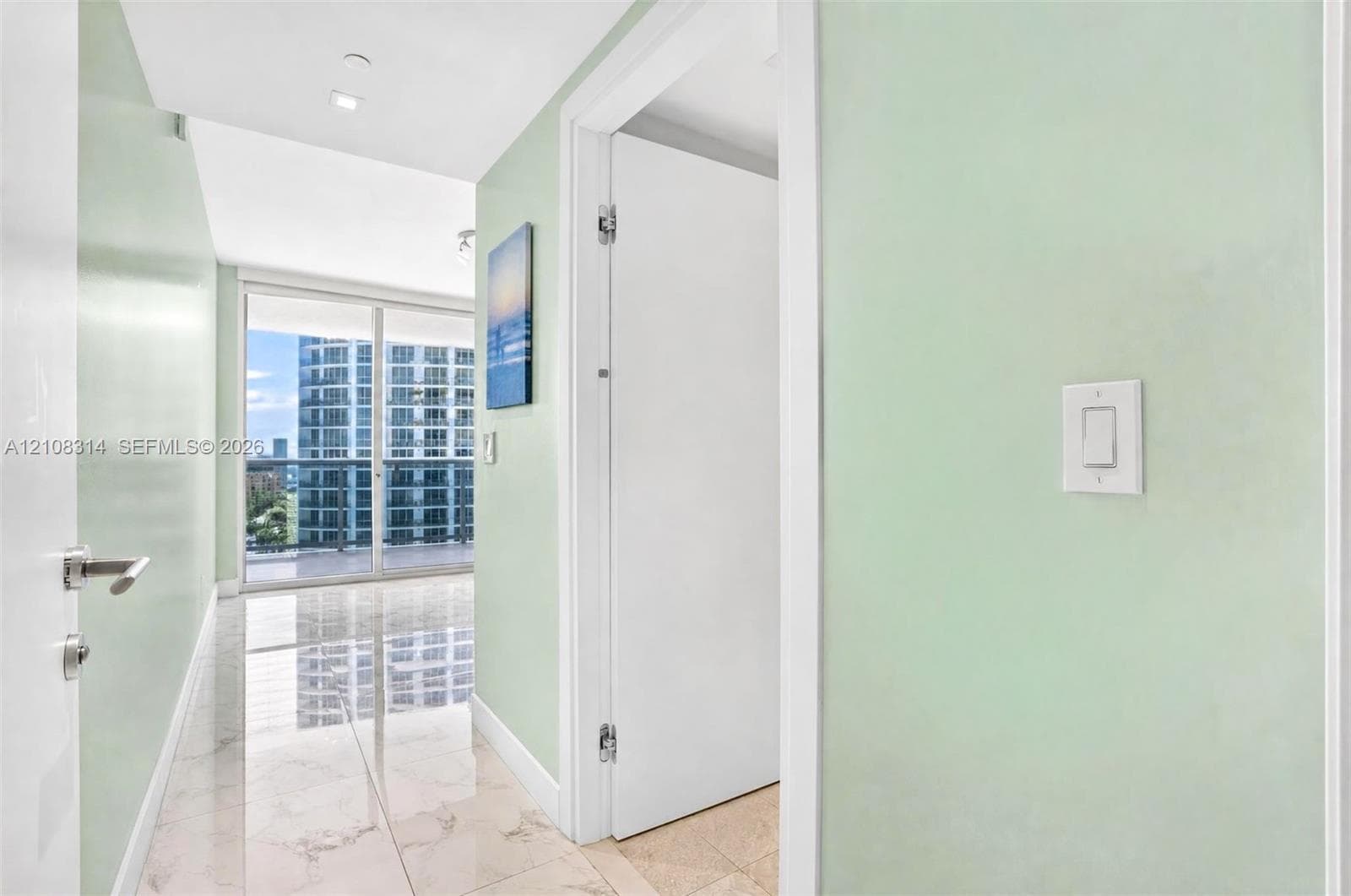 Hallway featuring large-format tile flooring, light-toned wall finishes, and floor-to-ceiling glass sliding doors