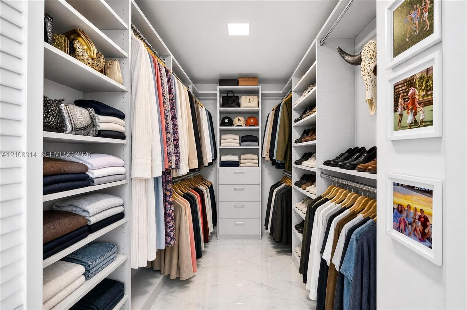Custom walk-in closet featuring extensive built-in white shelving, integrated clothing rods, a central storage tower with four pull-out drawers, and polished stone-finish flooring