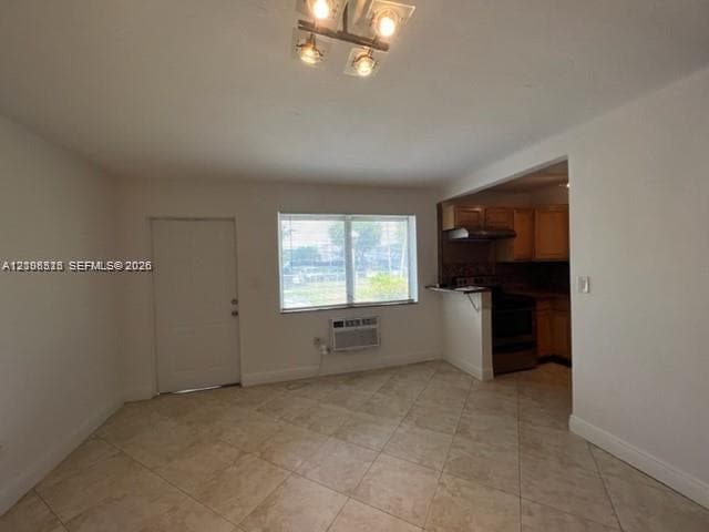 Neutral-toned tile flooring, four-light flush-mount ceiling fixture, and large single-hung window with an integrated wall-mounted air conditioning unit