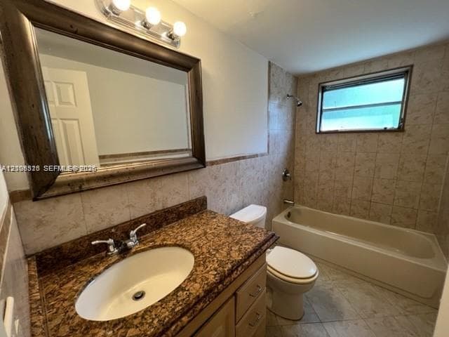 Bathroom featuring a vanity with a stone countertop, oval undermount sink, framed mirror with three-light fixture, tiled walls, and a shower-tub combination