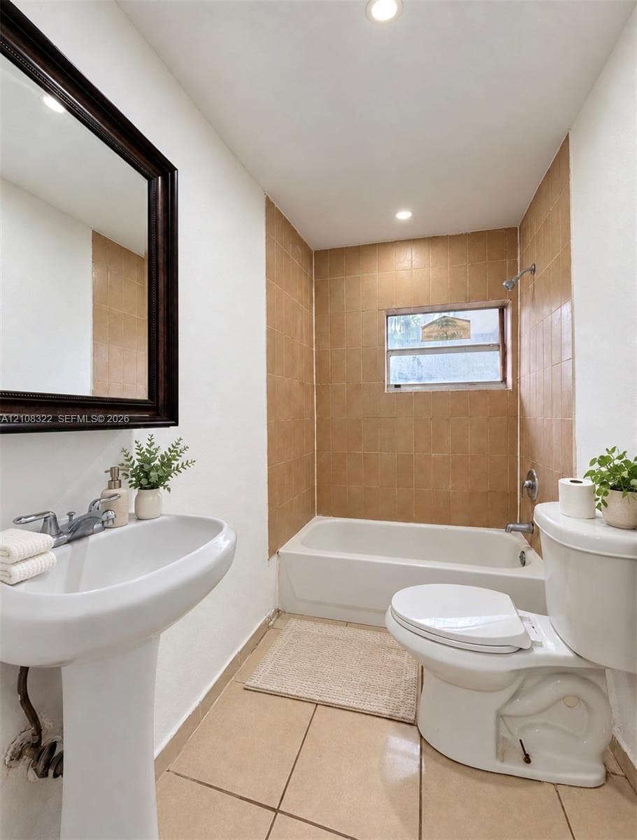 Bathroom featuring a pedestal sink, framed wall mirror, tiled bathtub surround, and tile flooring