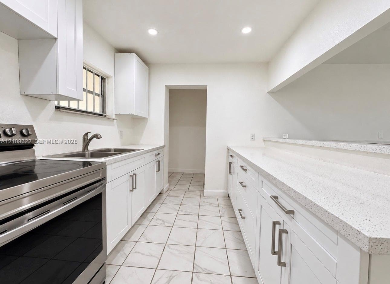 Kitchen featuring white cabinetry with brushed metal hardware, solid-surface countertops, recessed lighting, and tile flooring