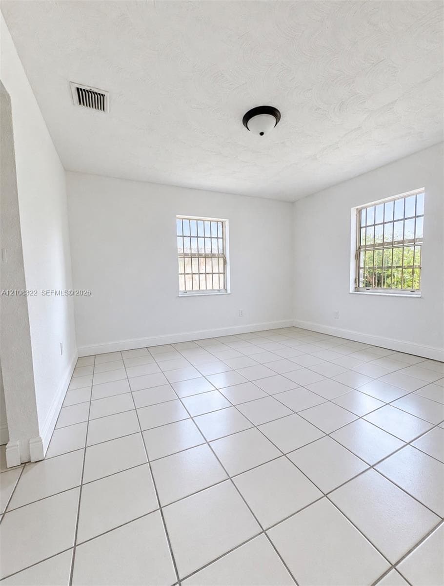 Neutral interior space featuring large-format ceramic tile flooring, two windows with metal security bars, and a central flush-mount ceiling fixture