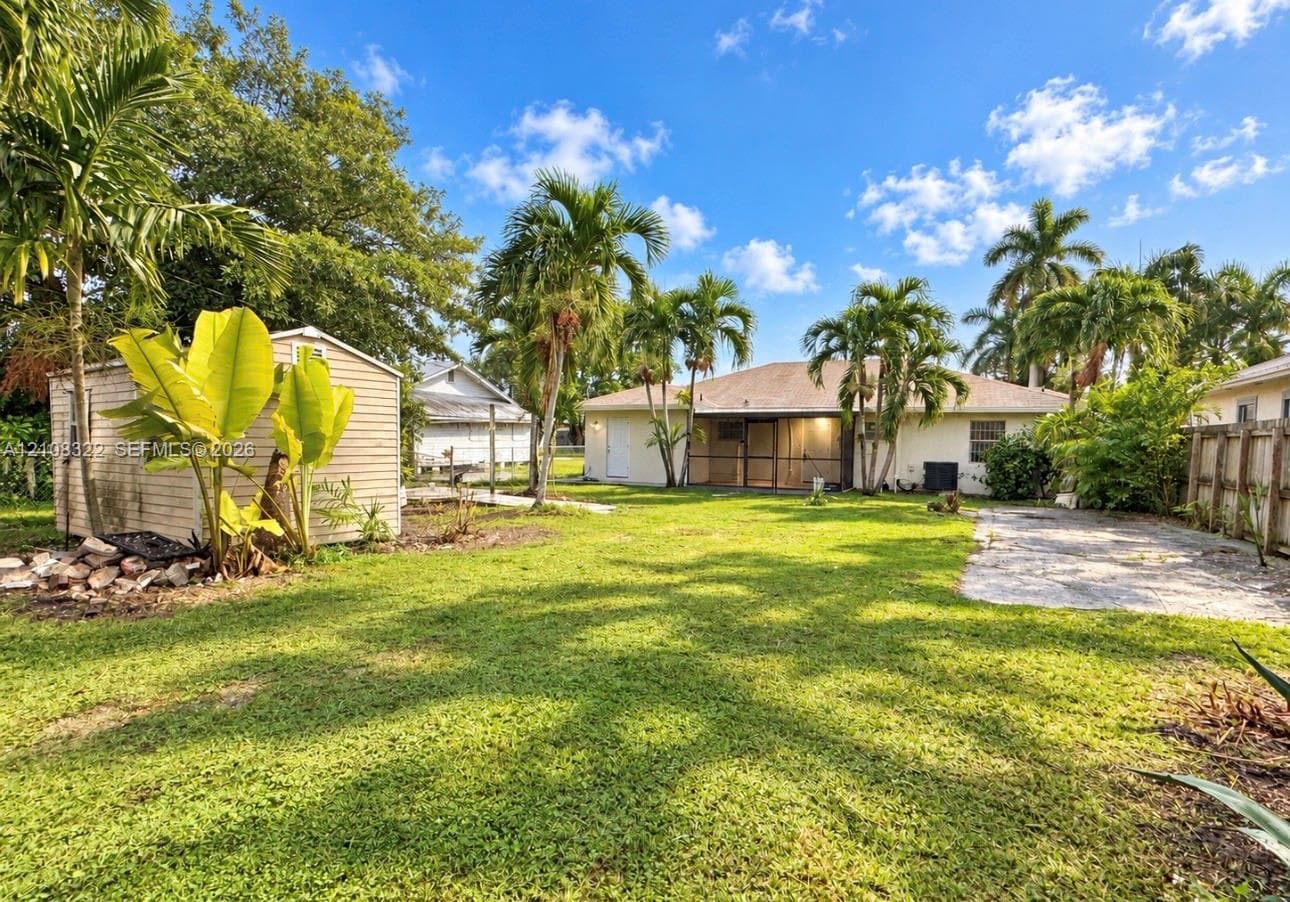 Expansive backyard featuring a detached storage shed, screen-enclosed patio, gravel driveway area, and mature palm trees