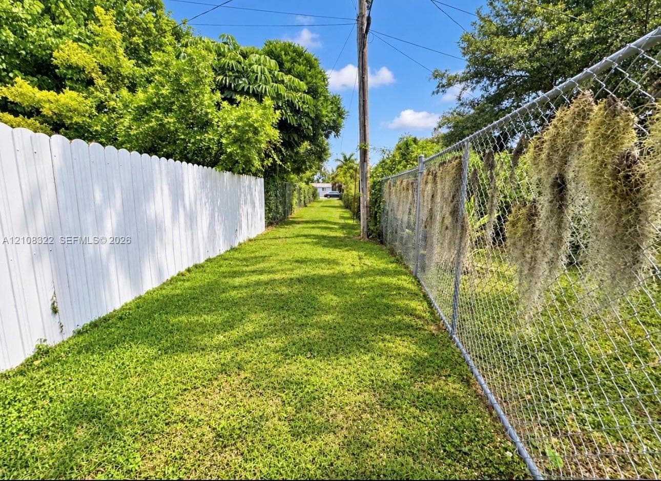 Expansive side yard featuring a manicured lawn, a solid white privacy fence, and a chain-link fence perimeter with mature trees