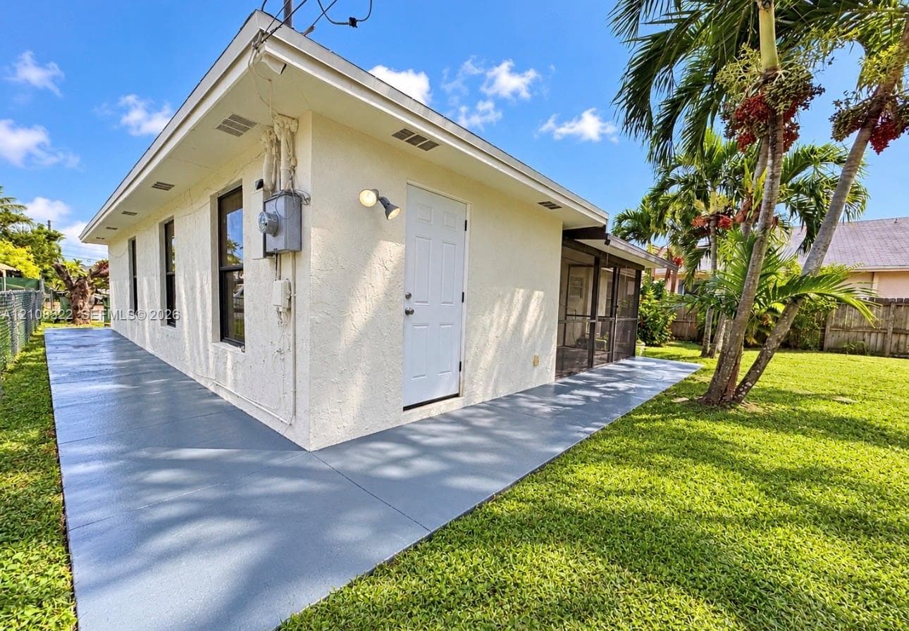 Stucco exterior featuring a wraparound concrete patio, screened-in porch, and expansive lawn with mature palm trees