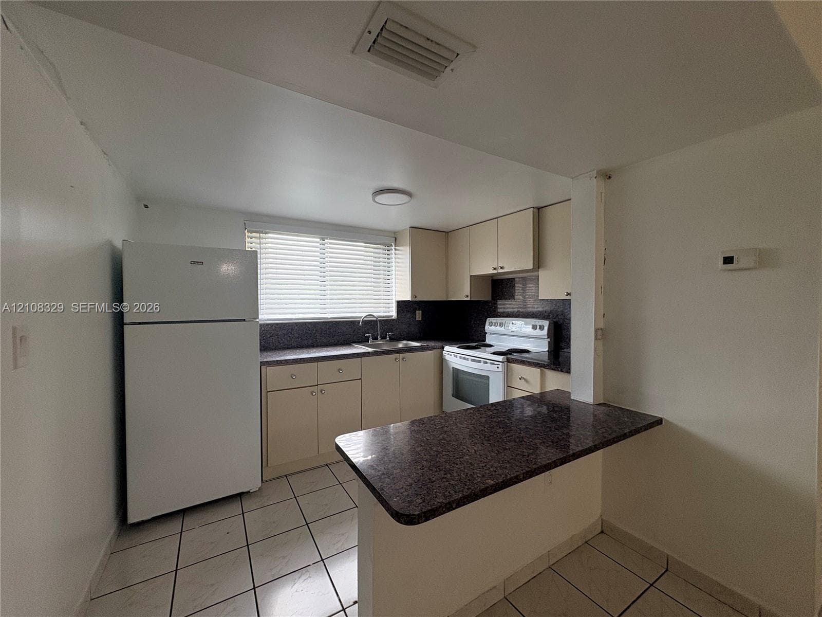 Kitchen featuring a peninsula with a dark countertop, white cabinetry, a top-mount sink, and tiled flooring