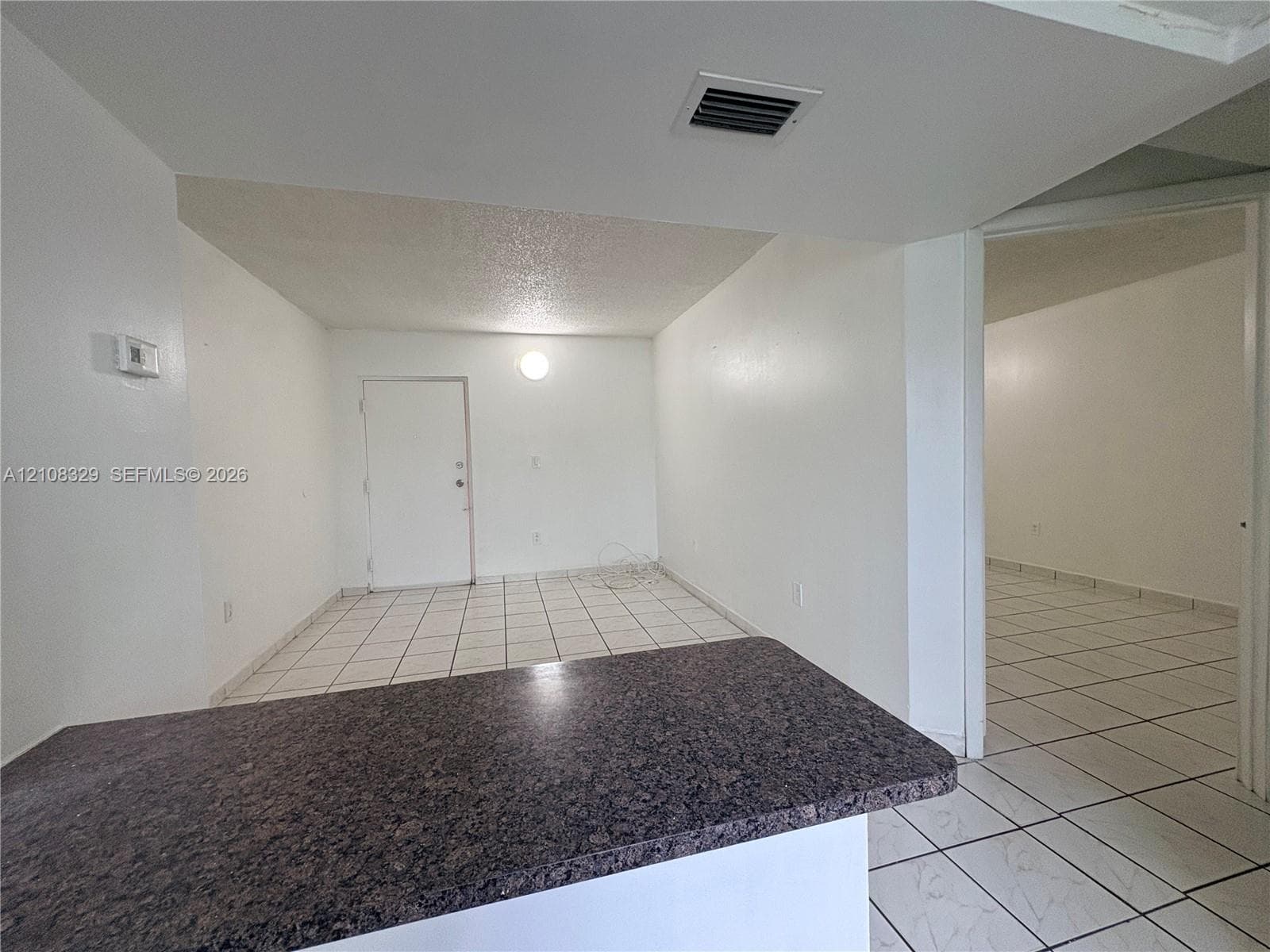 Interior space featuring neutral wall tones, white ceramic tile flooring throughout, and a stone-surface peninsula countertop