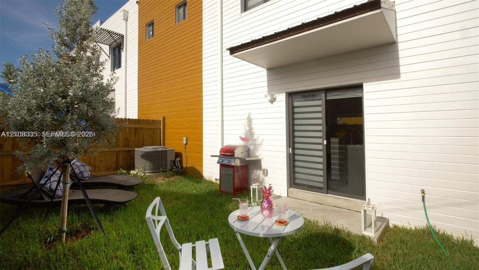 Exterior featuring horizontal white siding, wood-toned vertical paneling, sliding glass door with an overhanging awning, and private grass yard enclosed by wood fencing