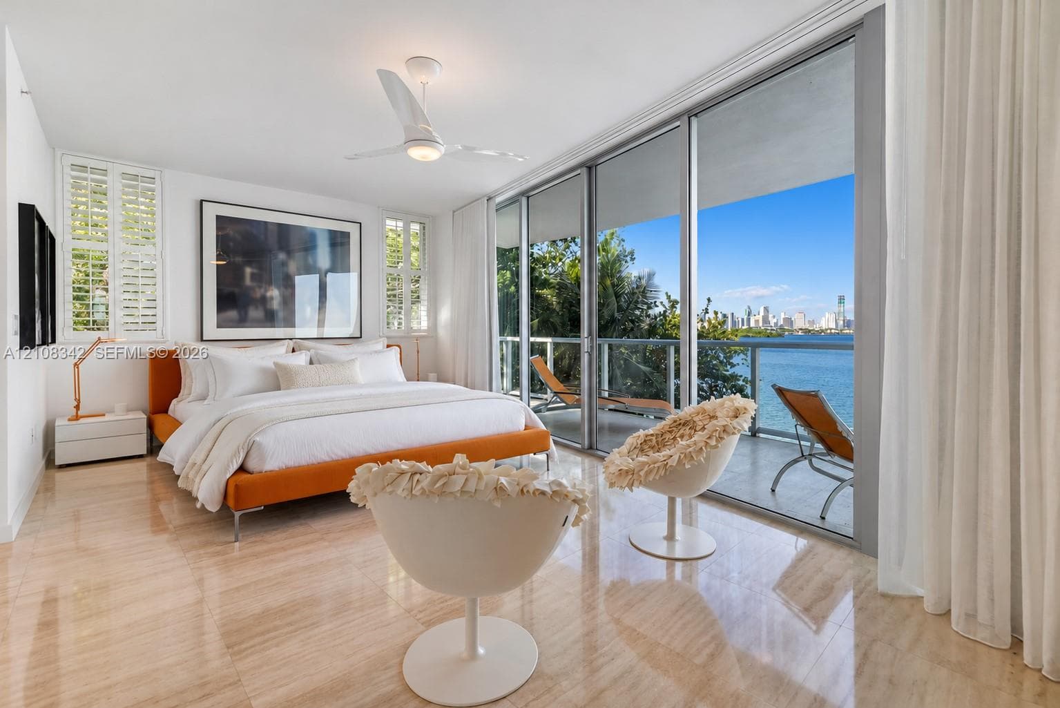 Polished stone flooring, floor-to-ceiling glass sliding doors, private balcony, three-blade ceiling fan, and plantation shutters