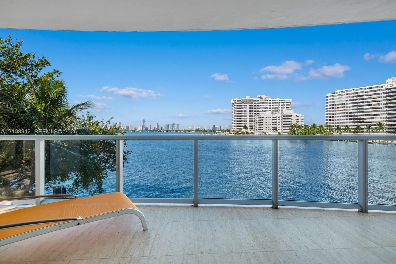 Covered balcony featuring stone flooring and a glass-paneled railing overlooking the water