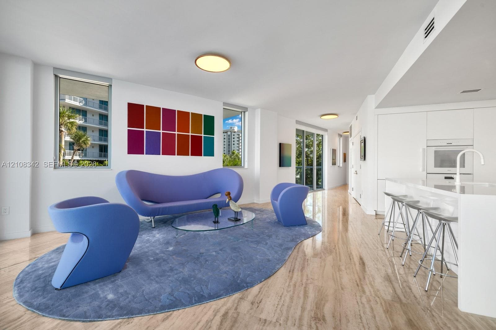 Open-concept interior featuring natural stone flooring, flush-mount circular lighting, expansive windows, and built-in minimalist cabinetry with integrated appliances