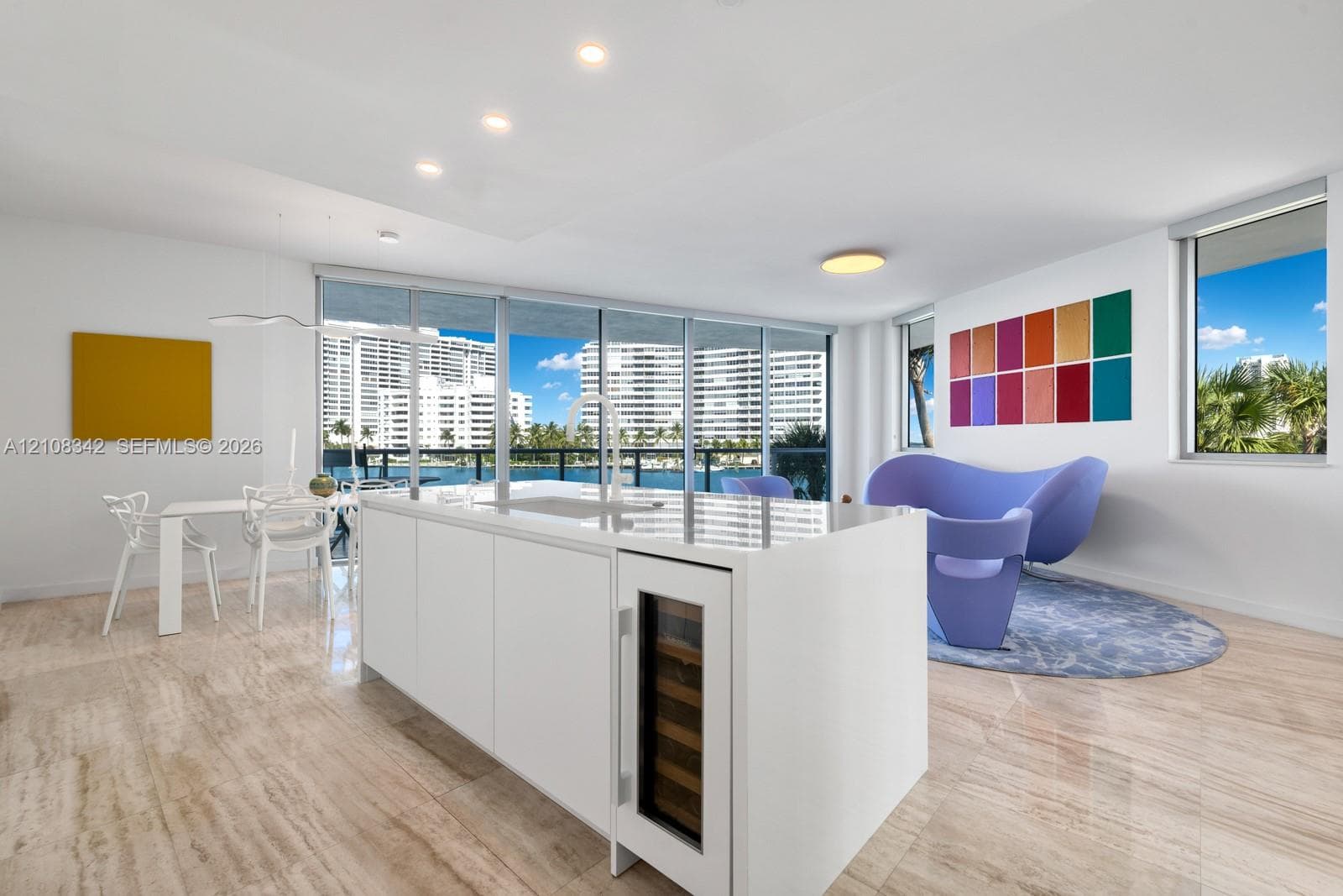 Kitchen island featuring a solid-surface countertop, built-in wine refrigerator, undermount sink, and minimalist cabinetry, complemented by stone-finish flooring, recessed lighting, and floor-to-ceiling windows