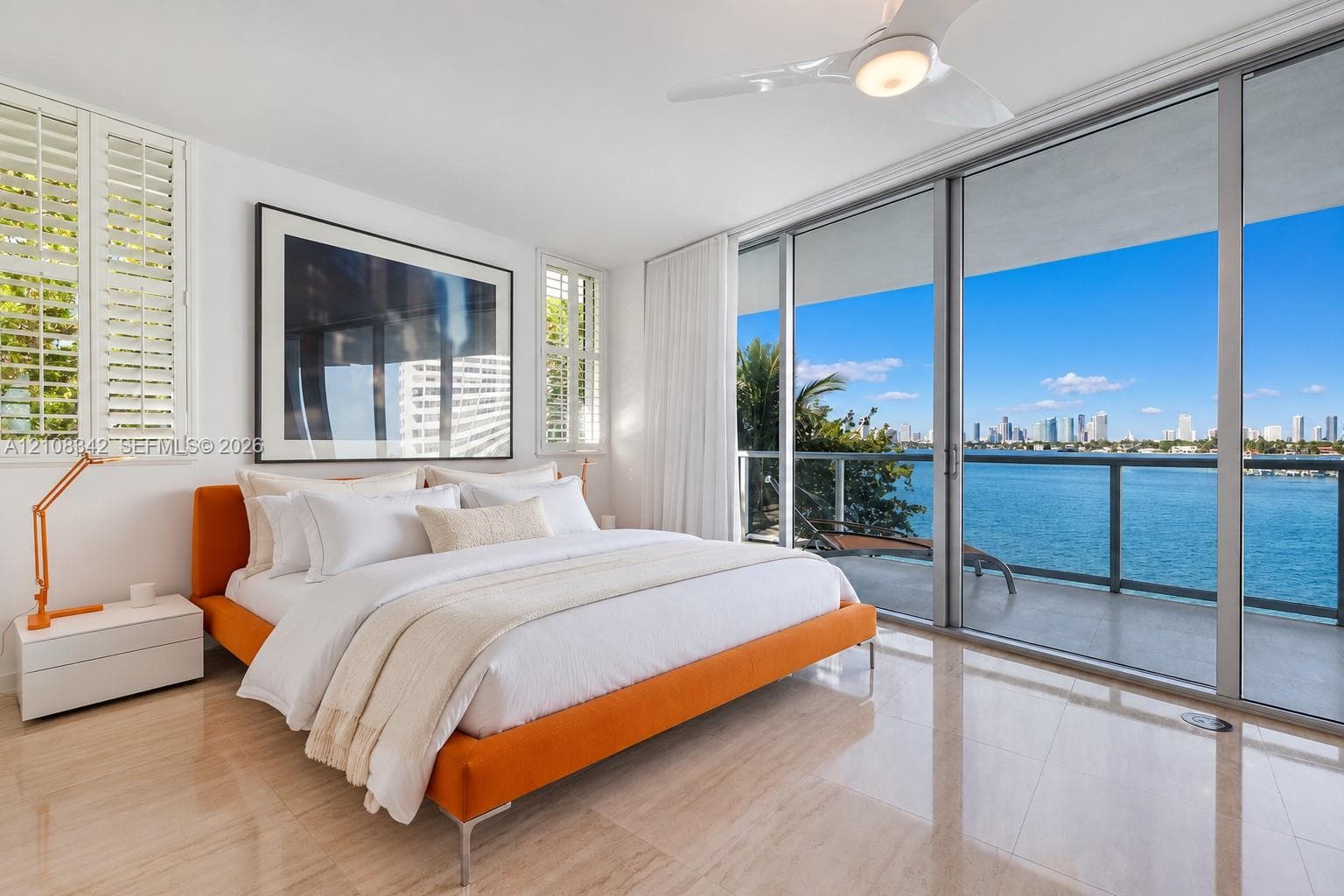 Floor-to-ceiling sliding glass doors, private balcony with metal railing, polished stone flooring, custom plantation shutters, and ceiling fan with integrated lighting