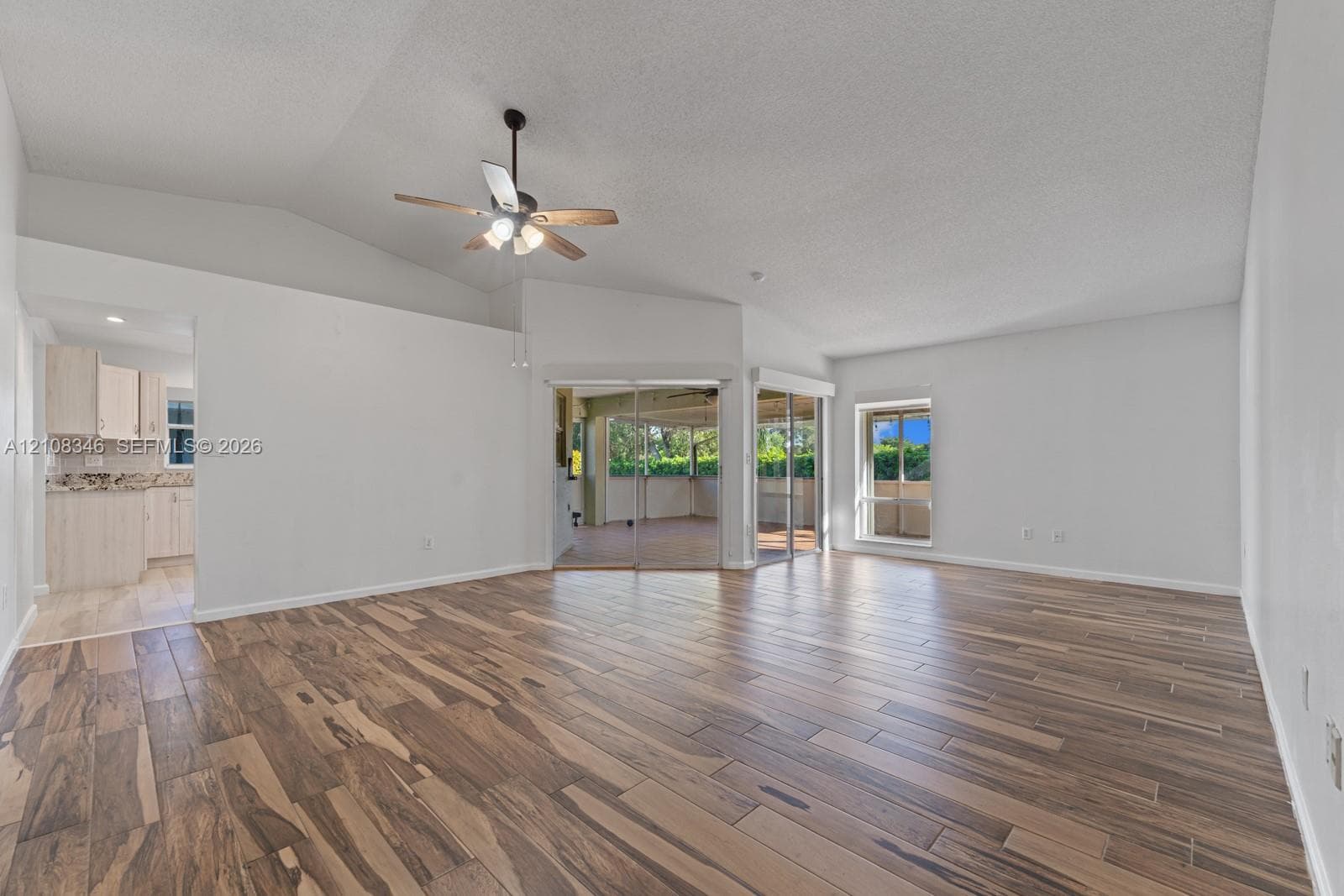 Living area featuring vaulted ceilings, wood-finish tile flooring, a ceiling fan with integrated lighting, and glass sliding doors
