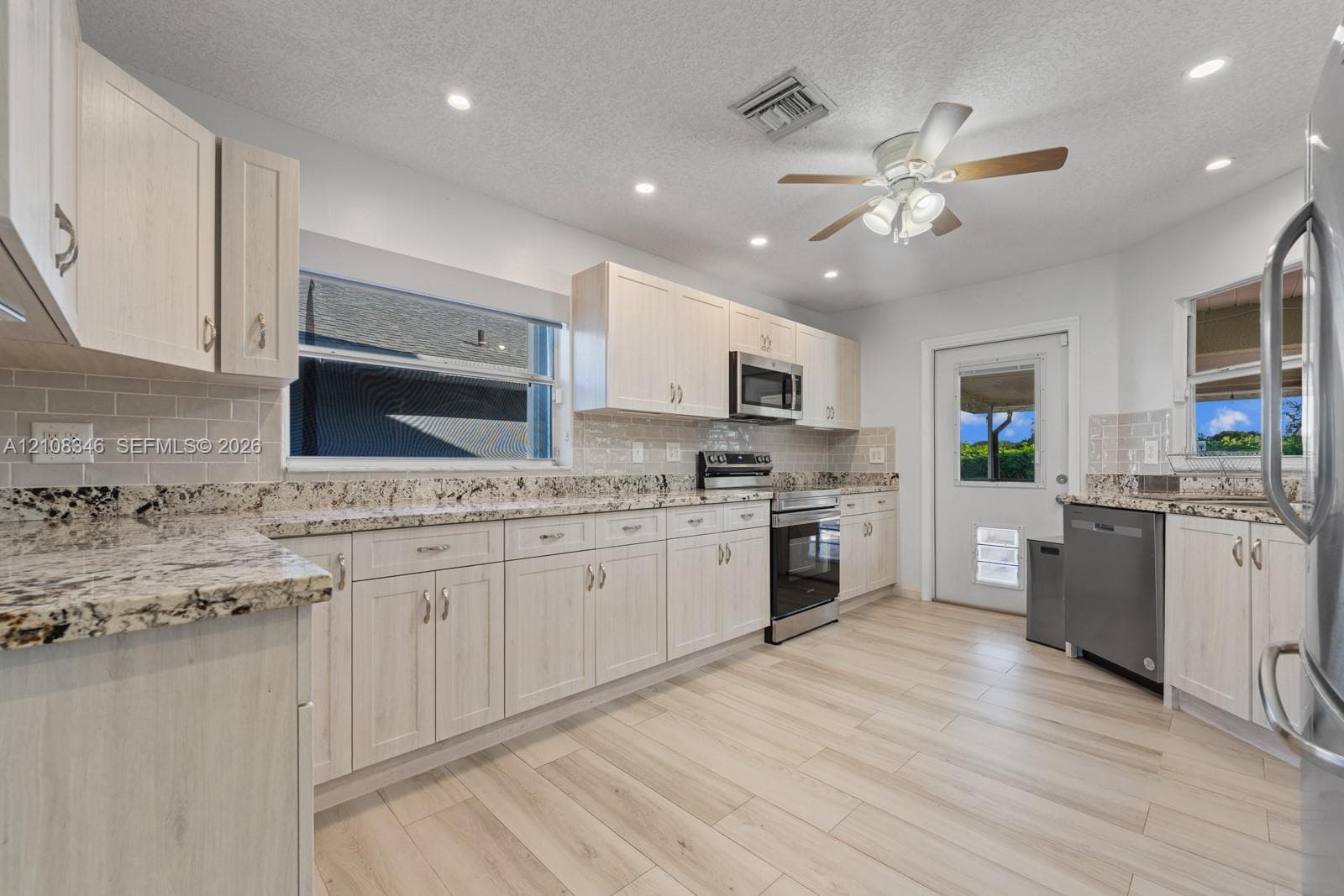 Kitchen featuring light-toned cabinetry, stone countertops, subway tile backsplash, stainless steel appliances, and wood-tile flooring