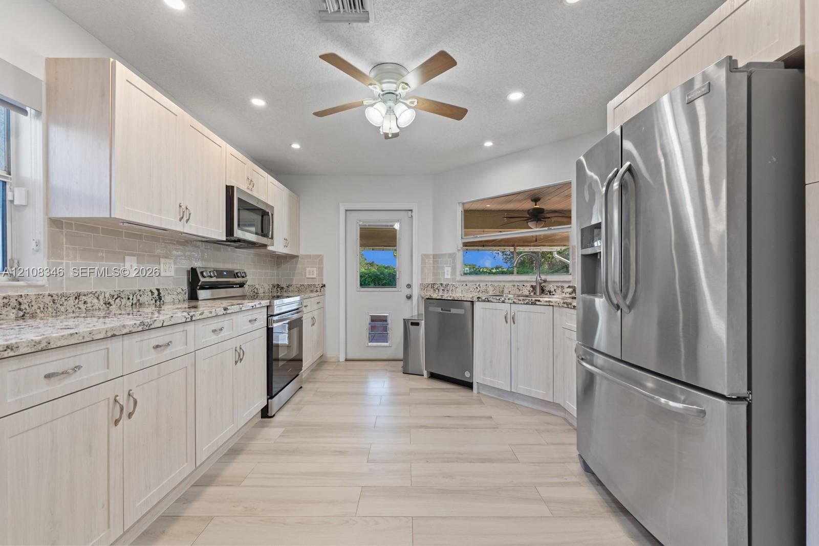 Kitchen featuring light-toned cabinetry, stone-finish countertops, stainless steel appliances, tile backsplash, and wood-tile flooring and exterior door to lani