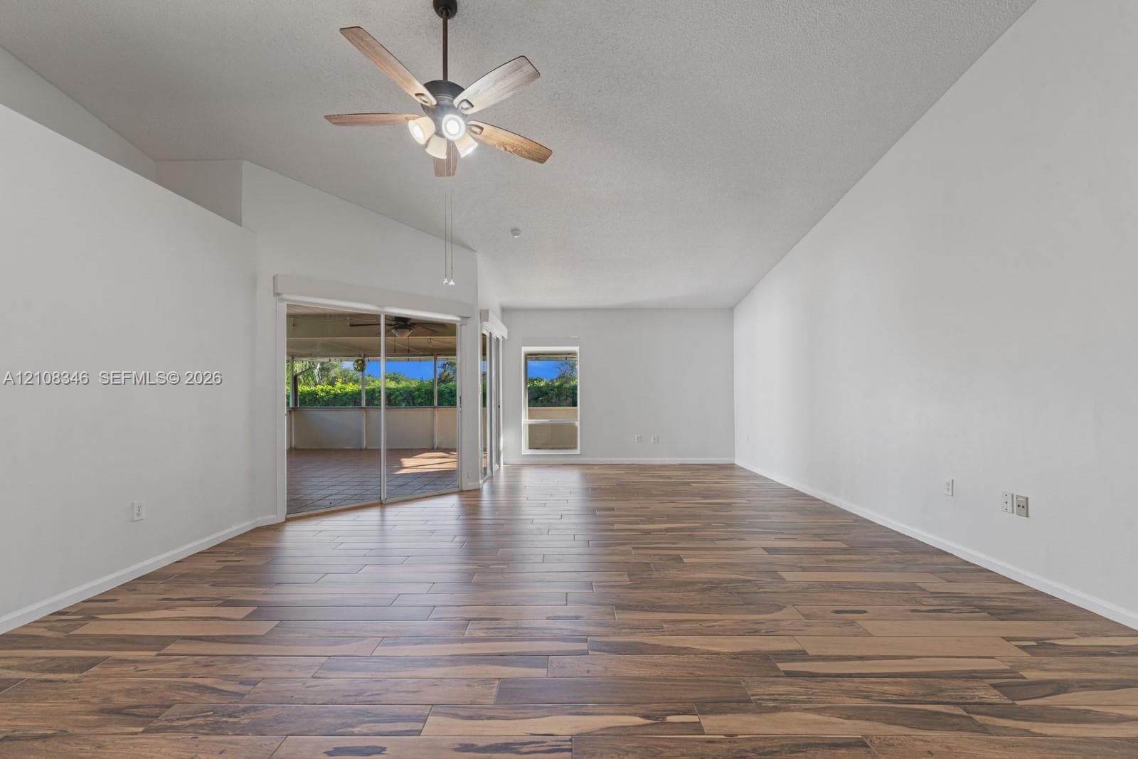 Vaulted ceilings featuring a five-blade ceiling fan with integrated lighting, wood-finish flooring, and sliding glass doors