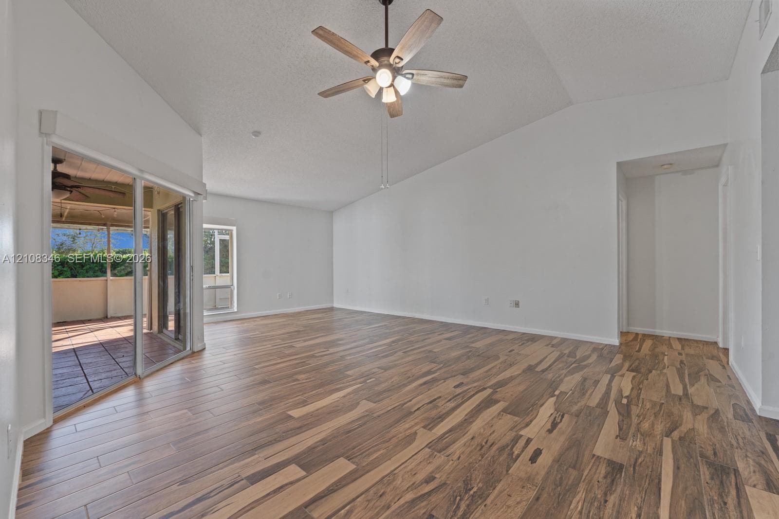 Vaulted ceilings, wood-finish flooring, ceiling fan with integrated lighting, and sliding glass doors