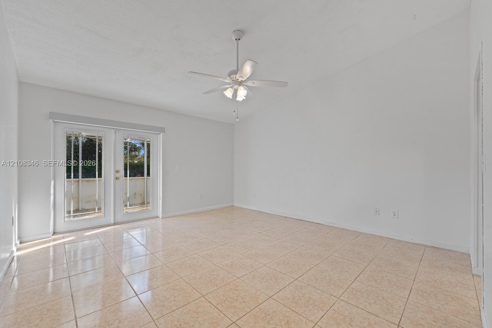 Spacious interior featuring neutral ceramic tile flooring, vaulted ceilings, a white ceiling fan with integrated lighting, and full-glass French doors