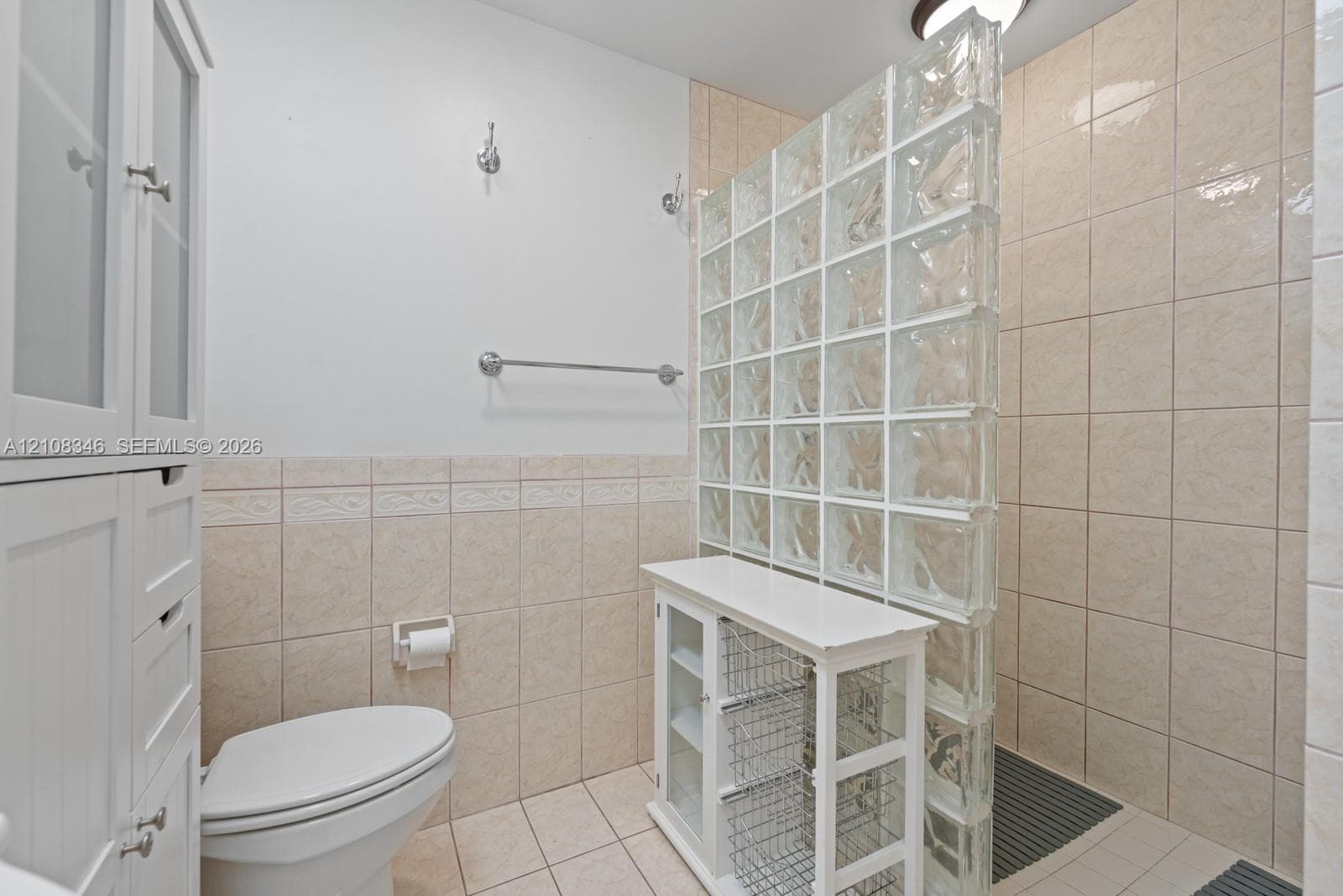 Glass block privacy partition, neutral wall-to-wall ceramic tile, built-in floor-to-ceiling cabinetry, and wall-mounted metal hardware