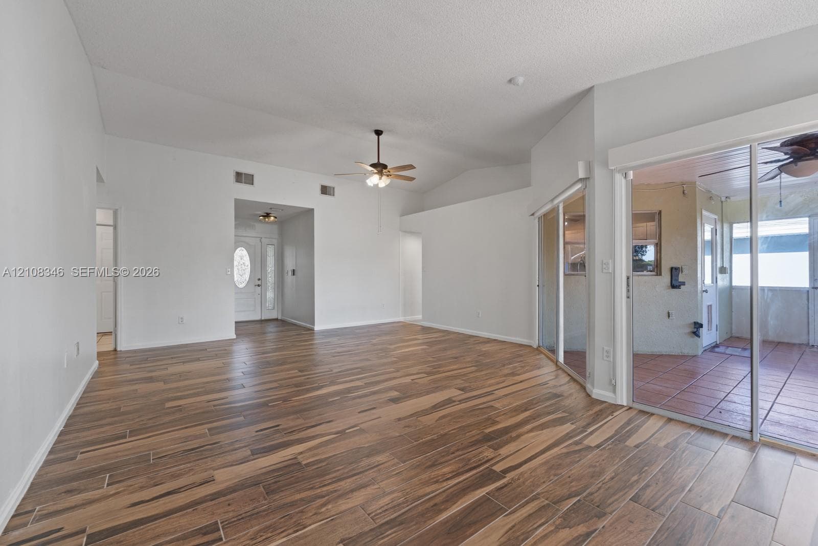 Open floor plan featuring vaulted ceilings, wood-finish tile flooring, ceiling fan with integrated lighting, and glass sliding doors