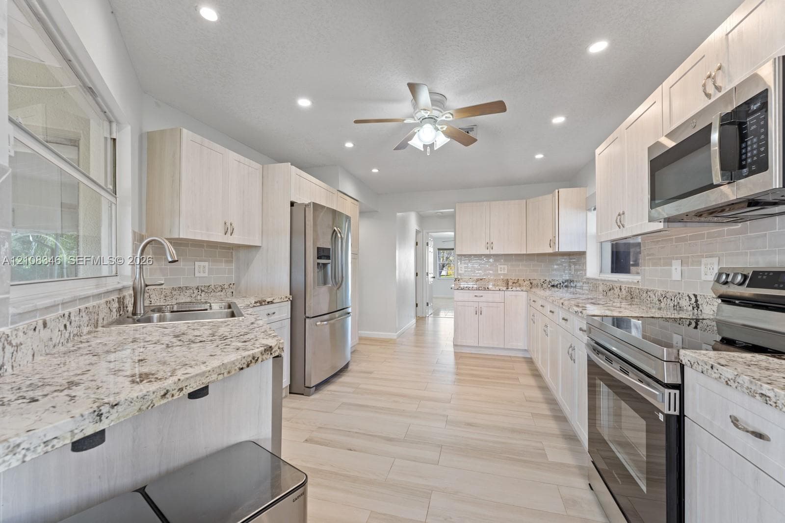 Kitchen featuring light-toned wood cabinetry, stone countertops, stainless steel appliances, subway tile backsplash, and wood-tile flooring
