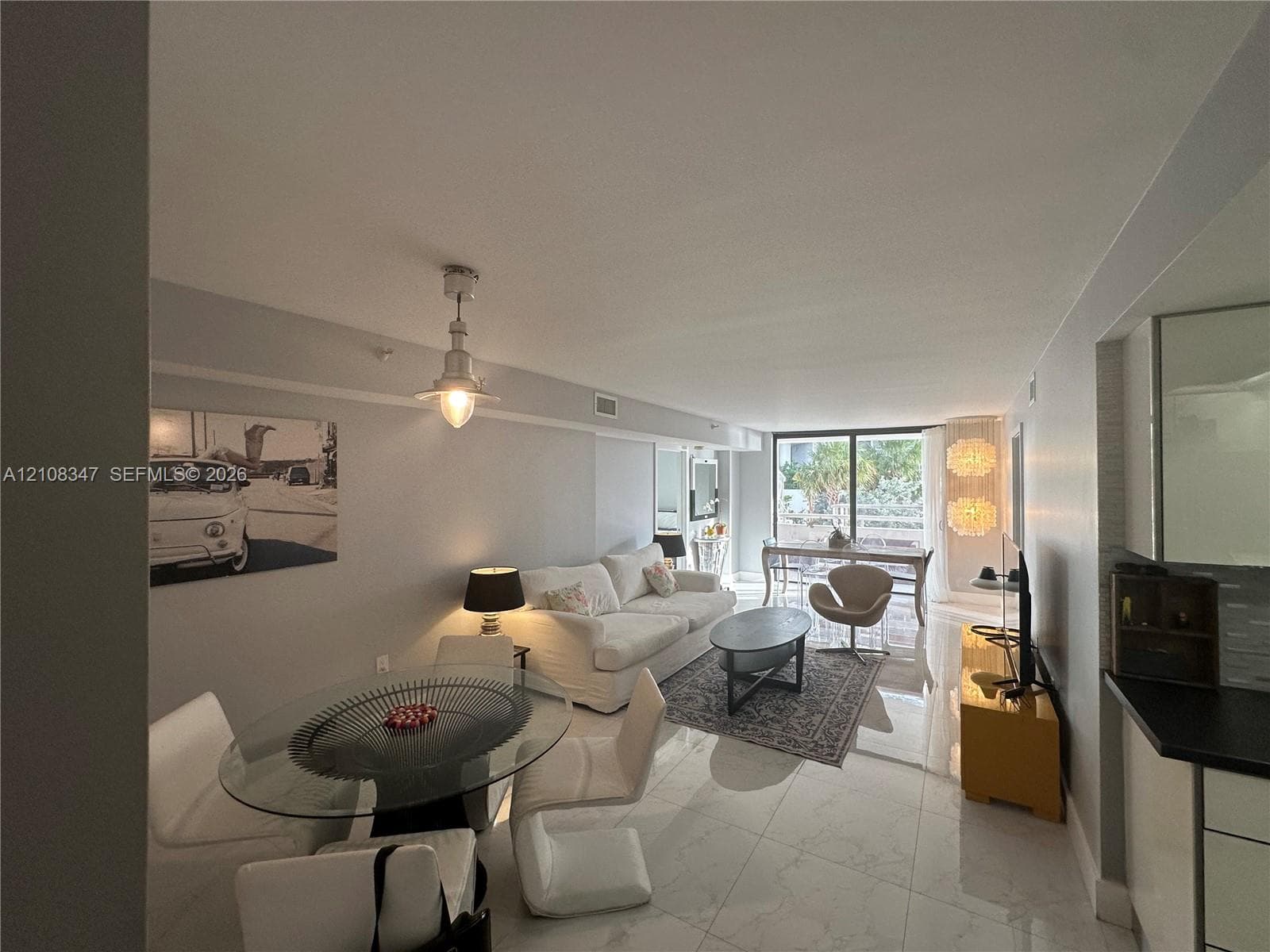 Open-concept living space featuring large-format tile flooring, industrial-style pendant lighting, and floor-to-ceiling glass doors