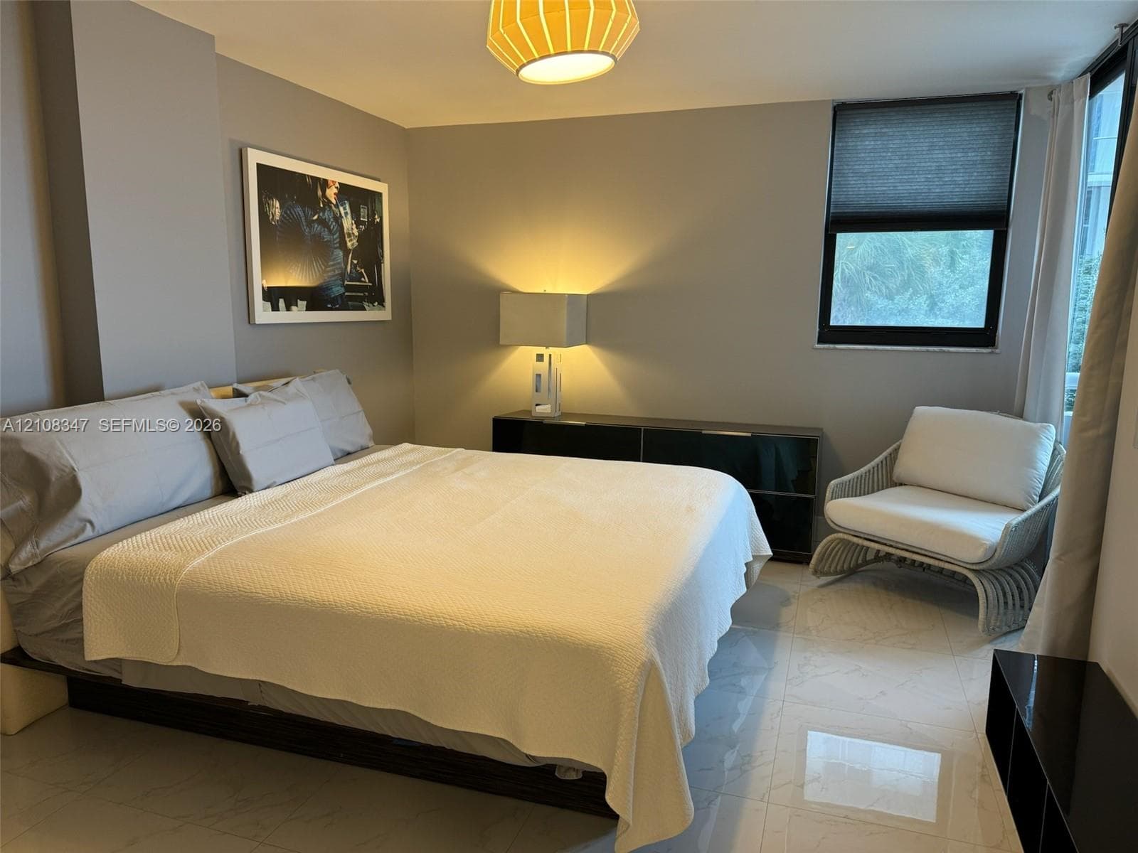 Neutral-toned room featuring large-format tile flooring, a window with a retractable shade, and a modern pendant light fixture