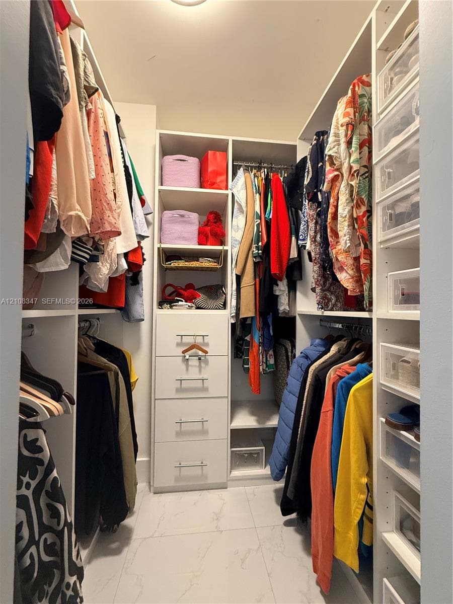 Walk-in closet featuring white built-in shelving, integrated dresser drawers with bar-pull hardware, hanging rods, and large-format tile flooring