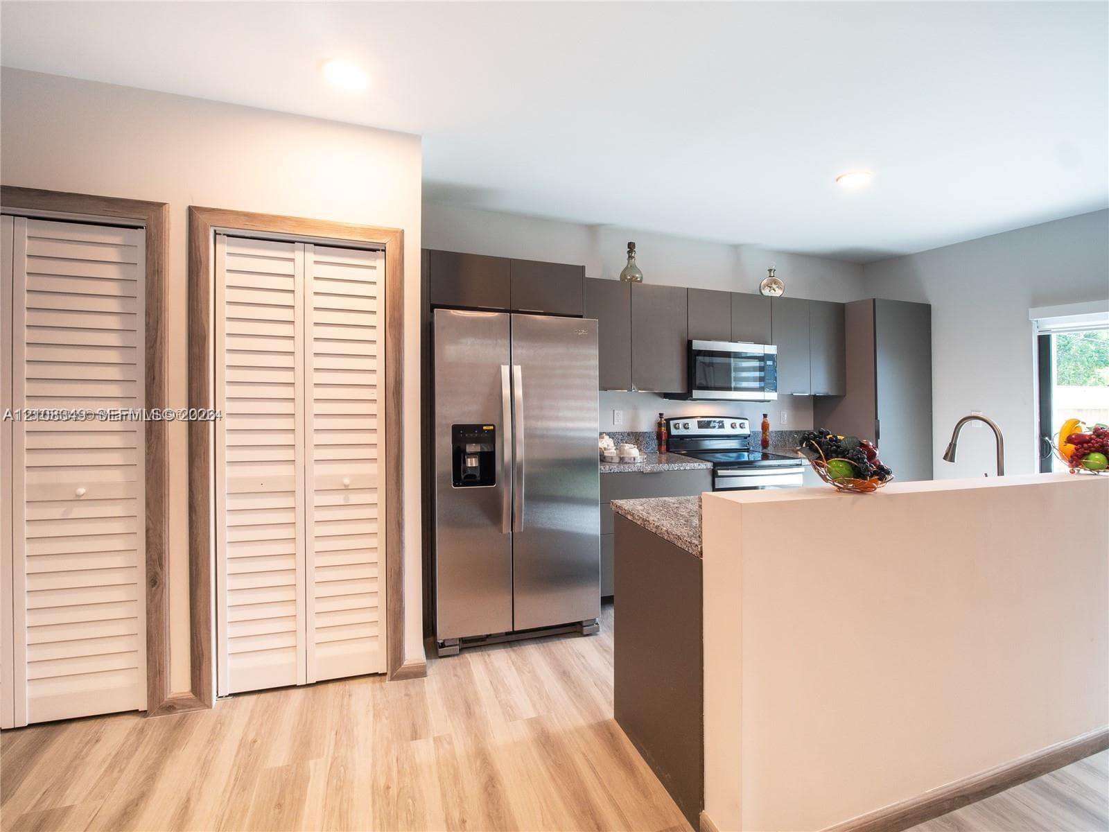 Kitchen featuring matte-finish cabinetry, stone countertops, stainless steel appliances, and wood-finish flooring, accompanied by dual louvered-door closets