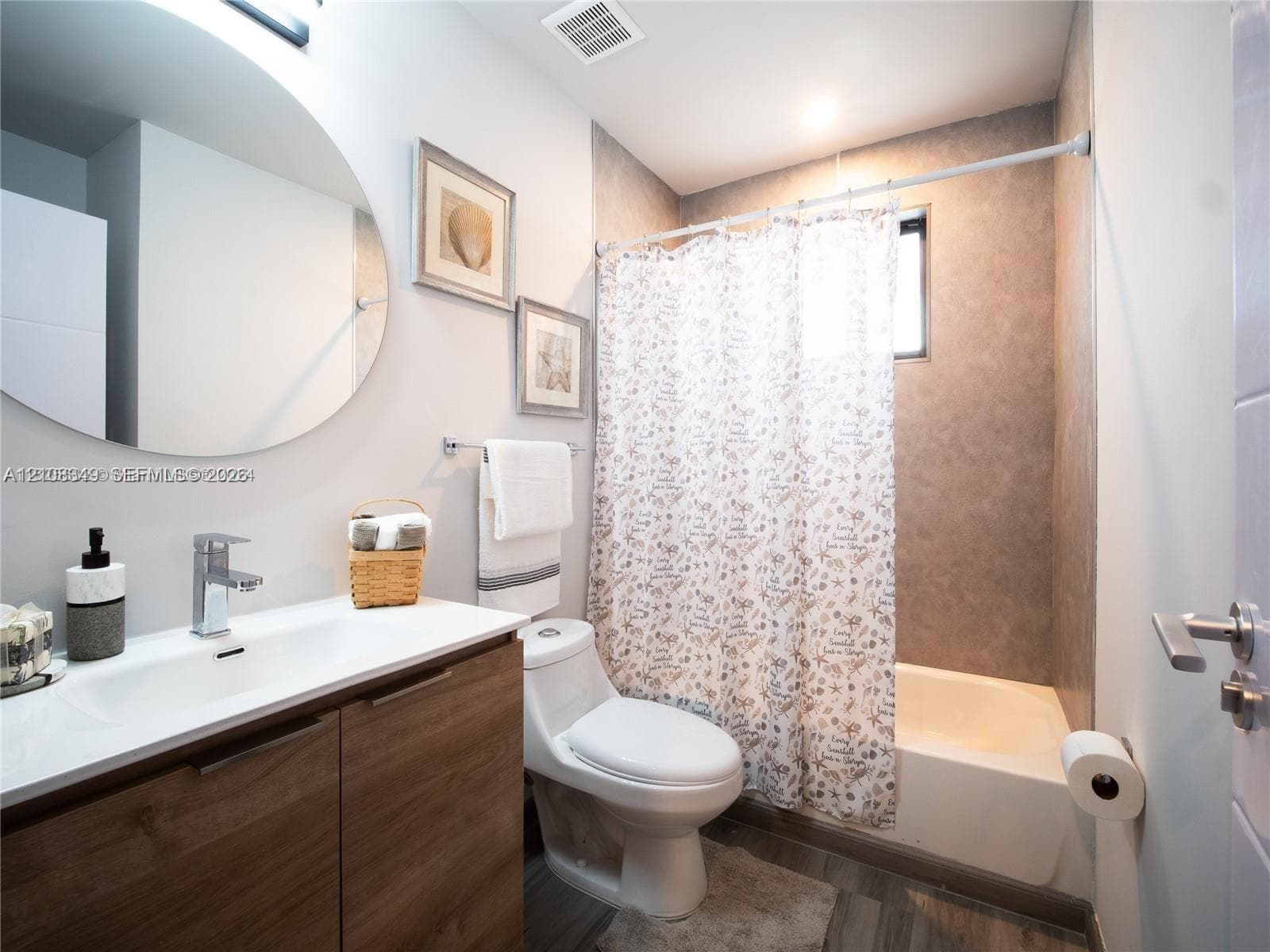 Bathroom featuring a wood-finish vanity with a rectangular sink, wall-mounted faucet, circular mirror, and a tub-shower combination with full-height tile surround