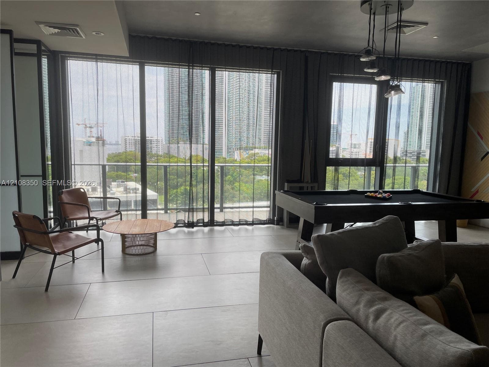 Floor-to-ceiling glass panel windows, large-format tile flooring, multi-pendant metal lighting fixture, and a railed balcony
