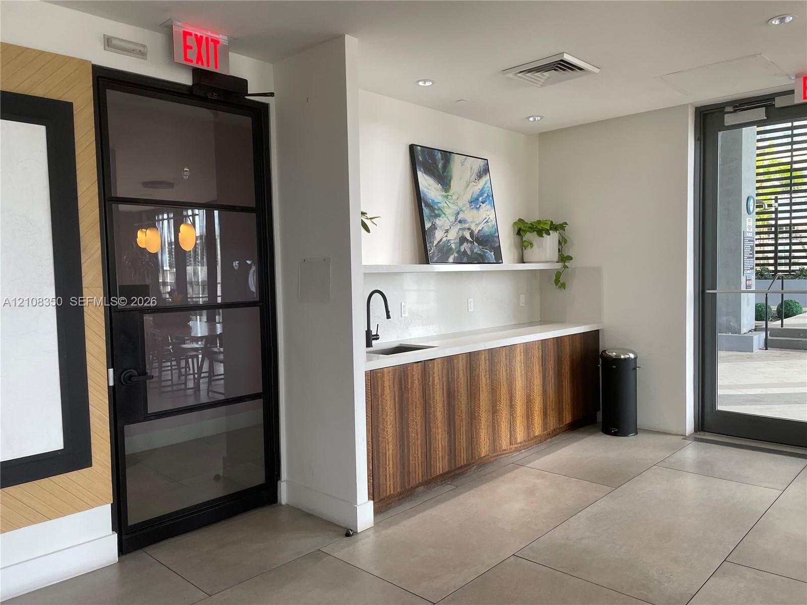 Built-in kitchenette featuring wood-veneer cabinetry, quartz countertop, and a matte black faucet, complemented by large-format tile flooring and an industrial-style metal-framed glass door