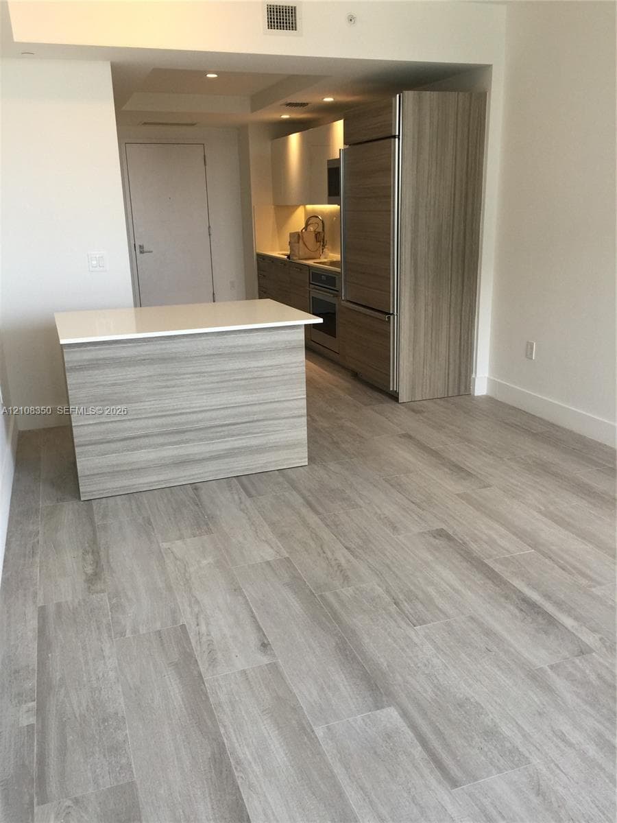 Kitchen featuring wood-finish cabinetry, a portable island with a solid-surface countertop, stainless steel appliances, and wood-finish flooring