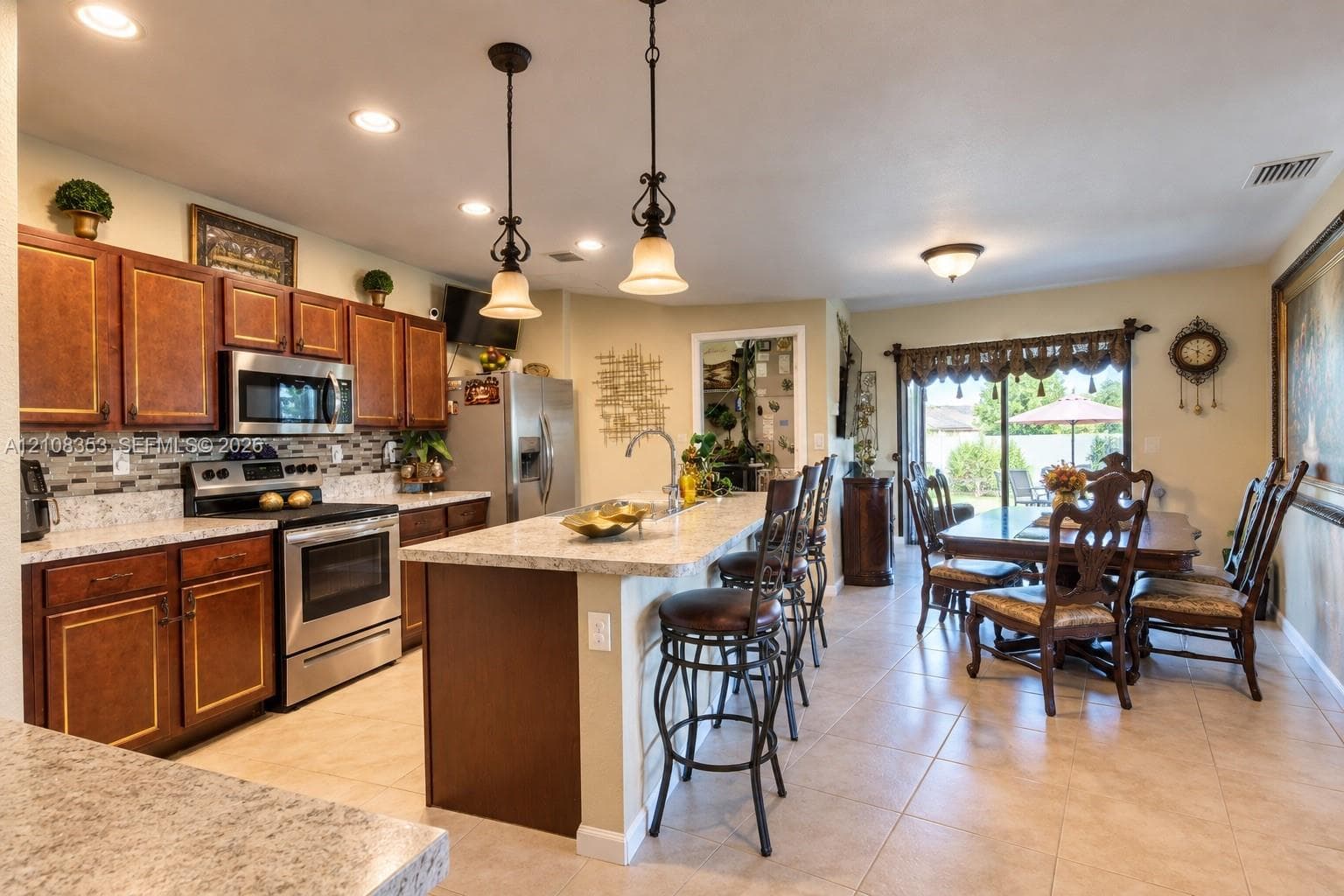 Kitchen featuring stained wood cabinetry, stone-finish countertops, tile backsplash, stainless steel appliances, and a central island with dual pendant lighting