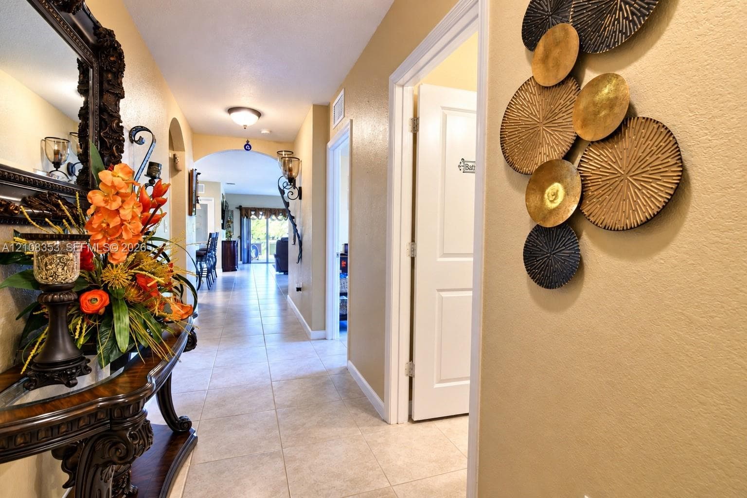 Interior hallway featuring tile flooring, arched entryways, and wall-mounted light fixtures