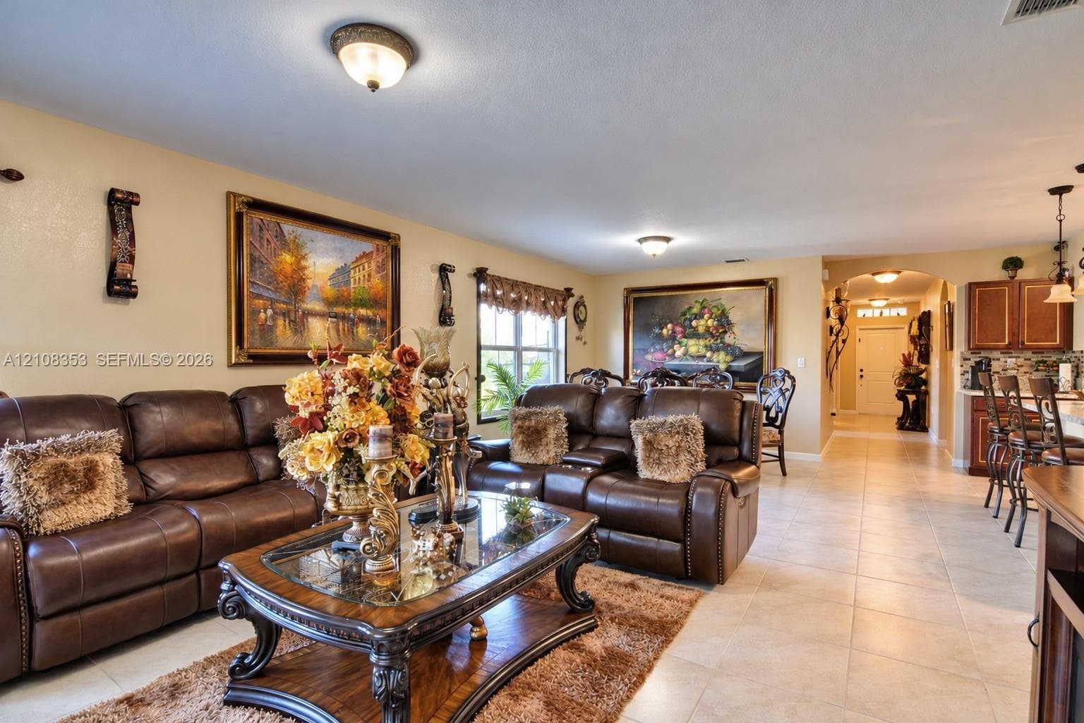 Open-concept interior featuring neutral tile flooring, recessed and flush-mount lighting, arched architectural detailing, and wood-finish cabinetry